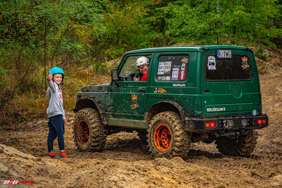 Zielone Suzuki Samurai na piasku, dziecko w niebieskim kasku macha do kierowcy