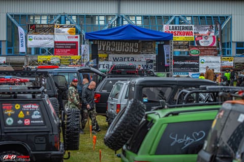 Parking terenówek przed halą z banerami sponsorów i niebieskim namiotem w bazie