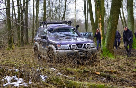 Fioletowy Nissan Patrol z bagażnikiem dachowym przedziera się przez leśne zarośla, obok uczestnicy