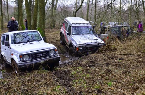 Biały Suzuki Samurai i oklejony Nissan Patrol grzęzną w błotnistym leśnym rowie