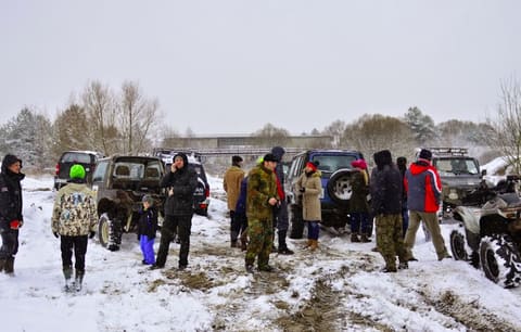 Grupa uczestników w zimowych kurtkach stoi przy terenówkach na zaśnieżonym placu