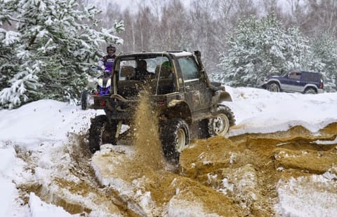 Suzuki Samurai bez dachu wyrzuca fontannę piasku na zaśnieżonym torze, za nim quad