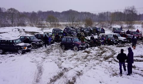 Około dwudziestu terenówek zebranych na zaśnieżonym polu podczas zimowego spotkania