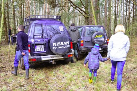 Kobieta z dzieckiem idzie za fioletowym Nissanem Patrol GR na leśnym postoju